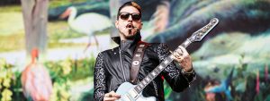 Scott Holiday playing guitar in front of a bird mural